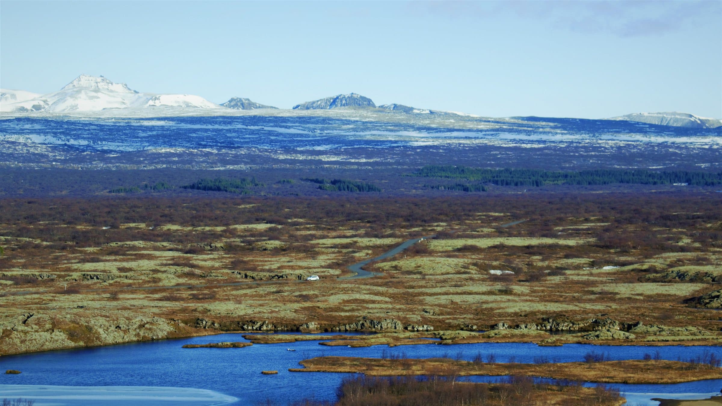 The rift valley plain at Þingvellir, lake and moss fields rising to snow-streaked mountains